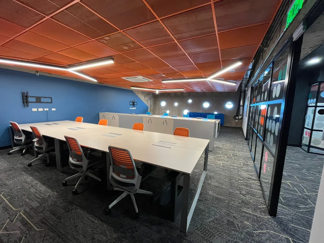 El cowork: una mesa larga con puestos de trabajo bajo un techo de paneles naranjos.