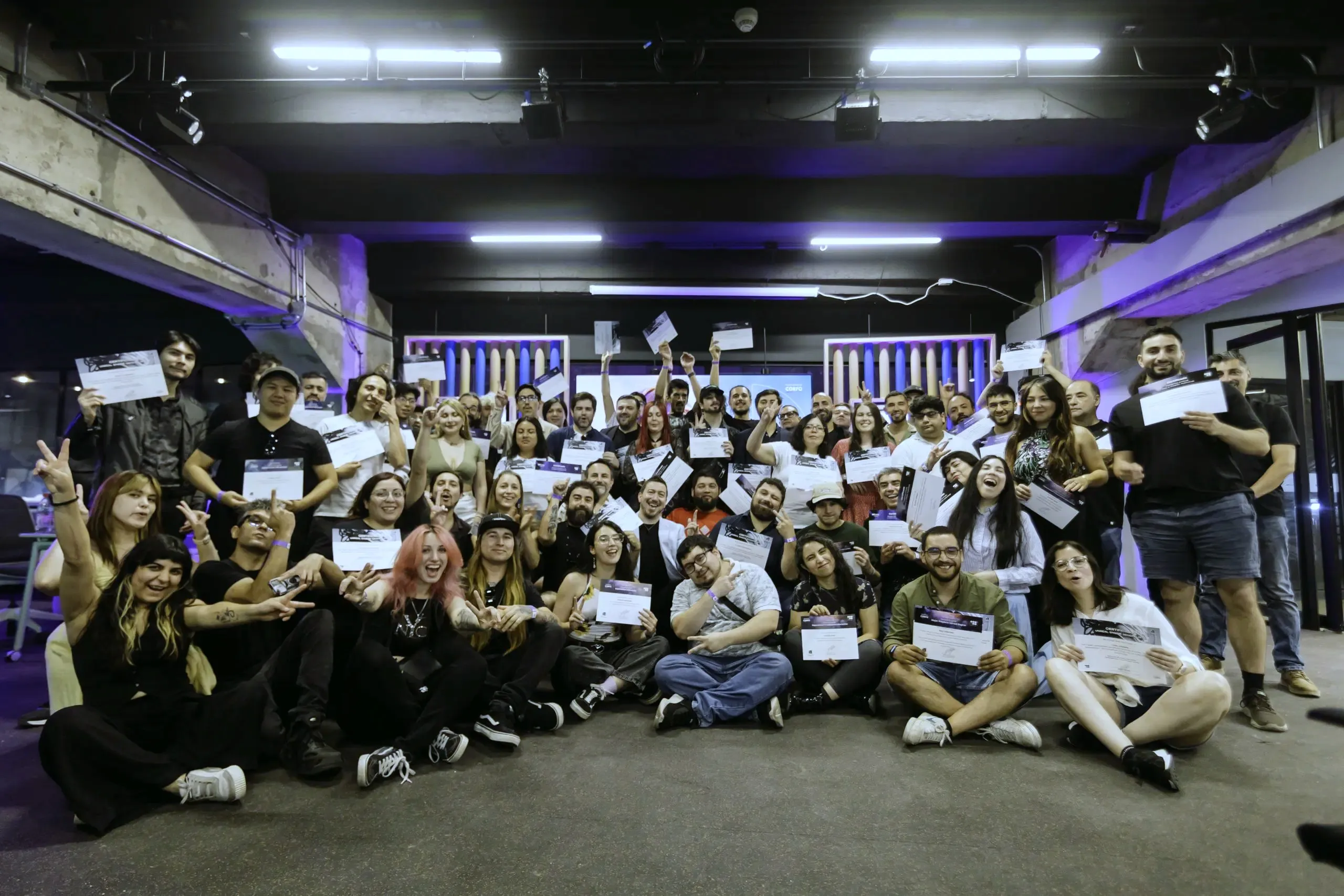 La comunidad del CRTIC celebrando una graduación en el laboratorio, con sus certificados en alto bajo la luz violeta del escenario.