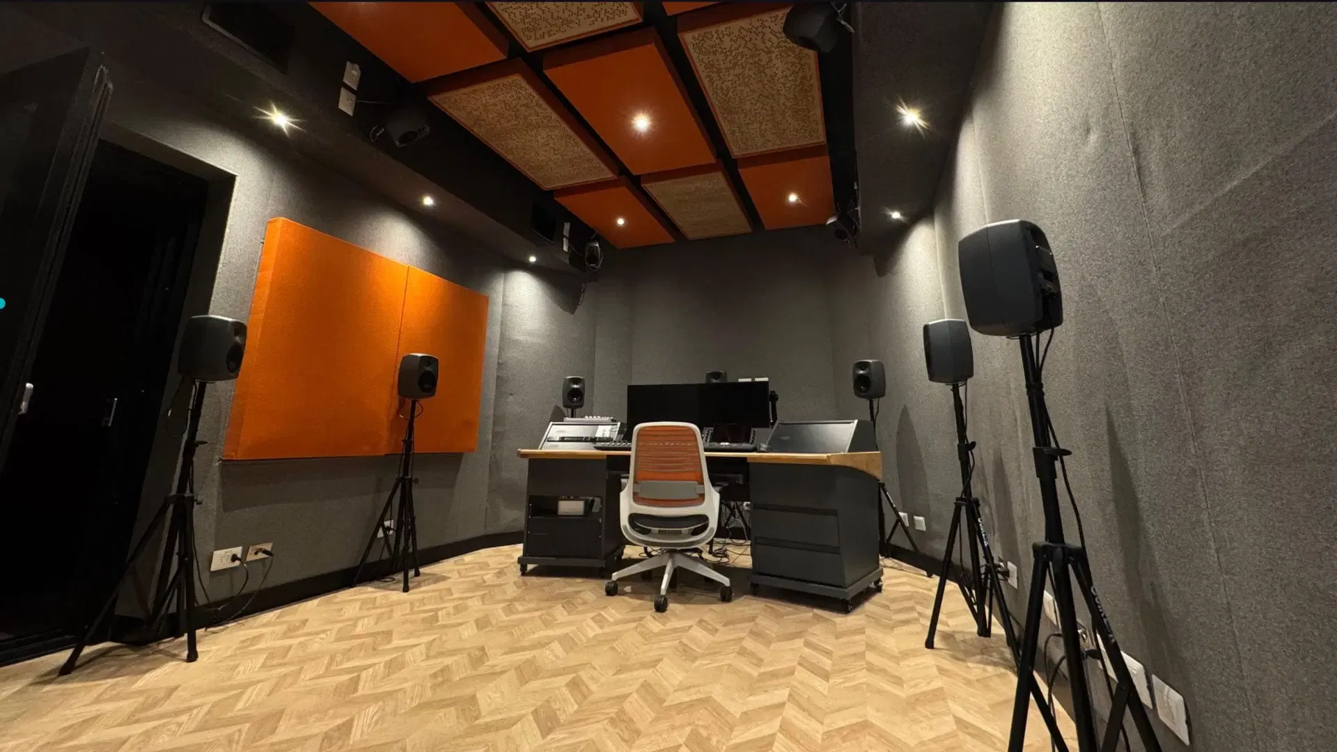 El estudio de audio inmersivo del laboratorio de Santiago: monitores en trípodes alrededor de una consola, con paneles acústicos naranjos en las paredes y el techo.
