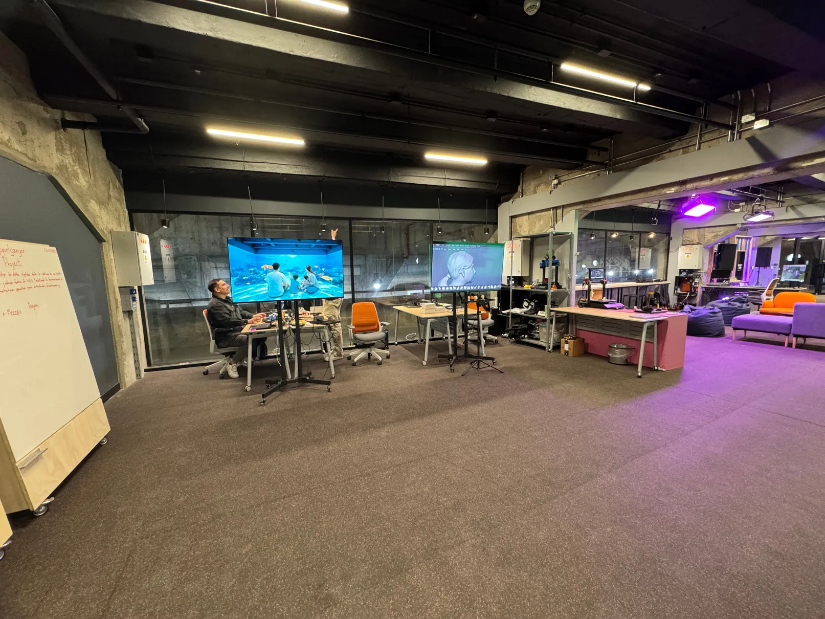 El StageLab: una sala amplia con mesas de trabajo, una pantalla al fondo y el croma verde a un lado.